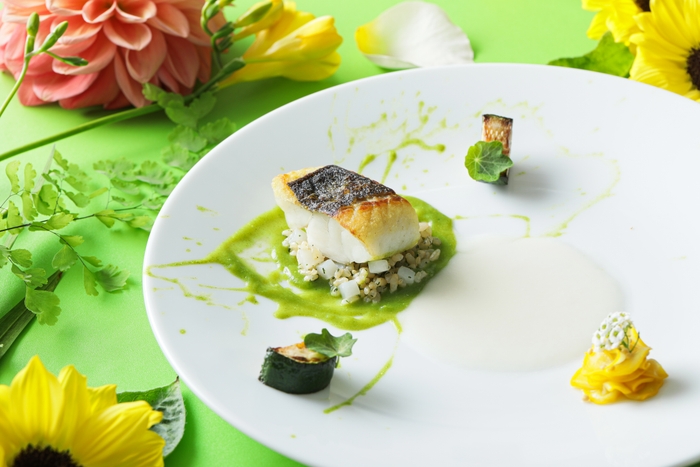 ▲愛知県産スズキのポワレと、ディルをアクセントにしたアオリイカとバター香る玄米ピラフを炒めをお客様の目の前で仕上げます。 夏が旬のズッキーニは、ピクルス・ロースト・ソース仕立てでご用意。