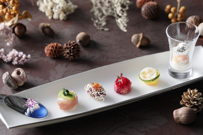 Hors-d’oeuvre】  〈ブルー〉甘みのあるマローブルーを酸味の効いたライムキャビアのはじける食感とともに  楽しめる一品。 〈グリーン〉春菊のほろ苦いソースがアクセントの一口大のお寿司。 〈パープル〉じっくり火入れした紫サツマイモにリンゴのカラメリゼとショウガのコンフィで    味わい豊かに仕上げました。 〈ルージュ〉サーモンのタルタルをローストビーツでサンドした見た目も鮮やかなジュエル風に 〈オレンジ〉甘みのあるアオリイカと白ワインでマリネしたサキイカを添えた季節野菜の    鈴かぼちゃと蓮根のサラダ仕立てで食感を楽しめます。 〈ホワイト〉イタリアの魚醤コラトゥーラがアクセントのズワイガニとカリフラワーのムース、ブーケのようにスライスしたカリフラワーを添えて華やかに。