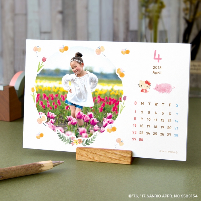 写真面のカレンダー部分にキティちゃんと動植物のモチーフが並び、花や蝶、フルーツなどがベストショットを可愛く縁取る丸枠フレーム