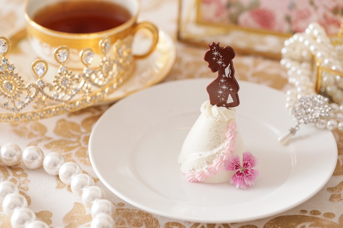 ▲プリンセスドレスケーキ イメージ ロイヤル ウエディングの主役である“プリ ンセス“をイメージした特別な一品。 優美な佇まいのプリンセスのドレス部分は、アーモンドムースといちごジュレの2層になっており、濃厚な甘みと爽やかな酸味が楽しめる。エディブルフラワーや銀粉でゴージャスなドレスのデティールを表現。