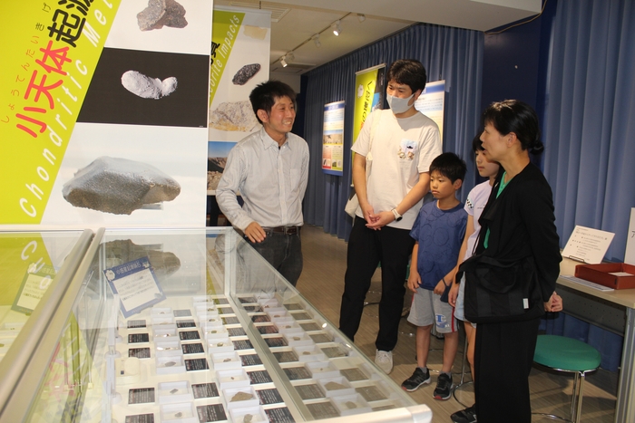 ギャラリートークで来場者に隕石を解説する新原准教授(中央)