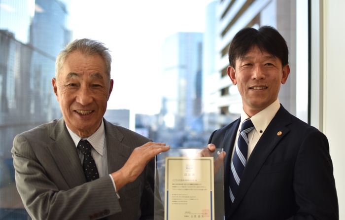 <認証書授与式の様子(左:UCDA理事長 在間 稔允 様、右:当社執行役員 下間 博仁)>