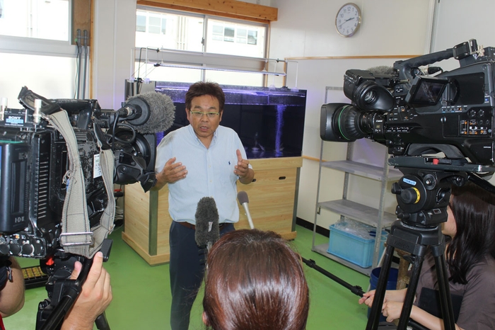 大型水槽前で報道陣の取材に答える山本准教授