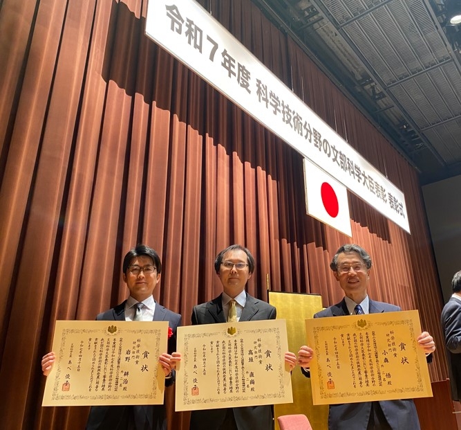 文部科学省で4月15日に行われた表彰式で、賞状を手に記念写真に納まる（左から）岩野准教授、高垣教授、小森名誉教授