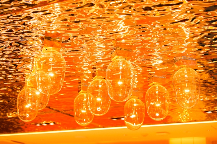 「廻転鮨 銀座おのでら本店」内装/波、イカ釣り舟の明かりを彷彿とさせる天井、夕陽をイメージした橙色の壁