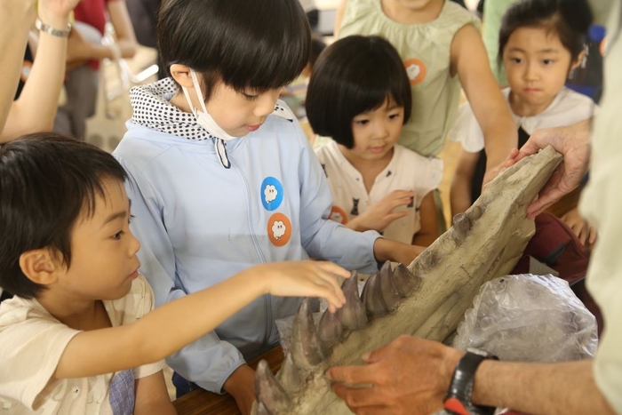 恐竜化石のレプリカに触ってみる子どもたち